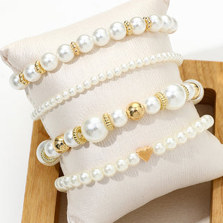 Four pearl-look bracelets with gold-tone accents on a display cushion